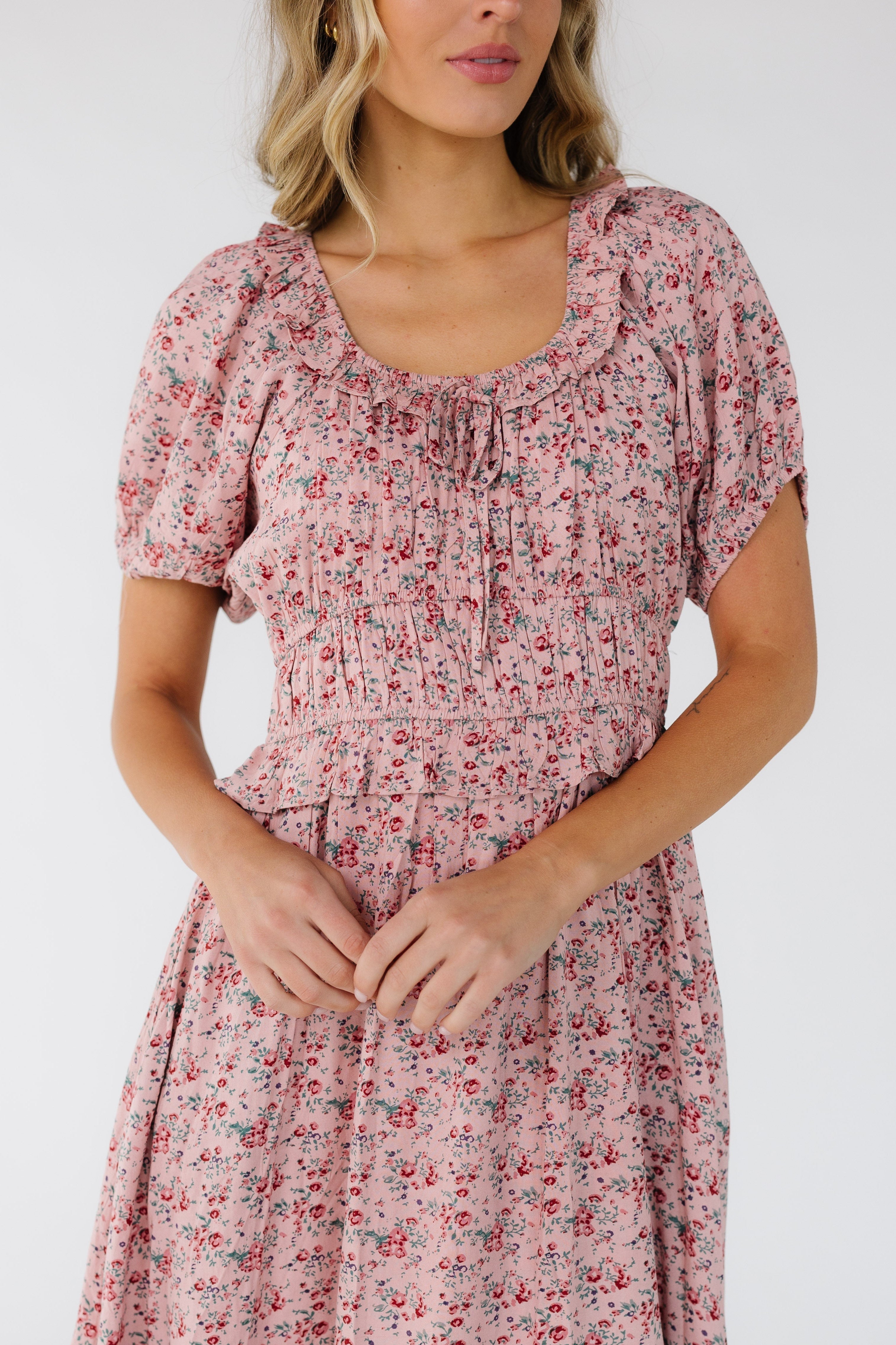 Close_view_of_a_woman_wearing_a_pink_floral_dress_with_a_wide_waistband_a_ruffled_scoop_neckline_and_short_puff_sleeves.jpg Citrus Jena Print Dress