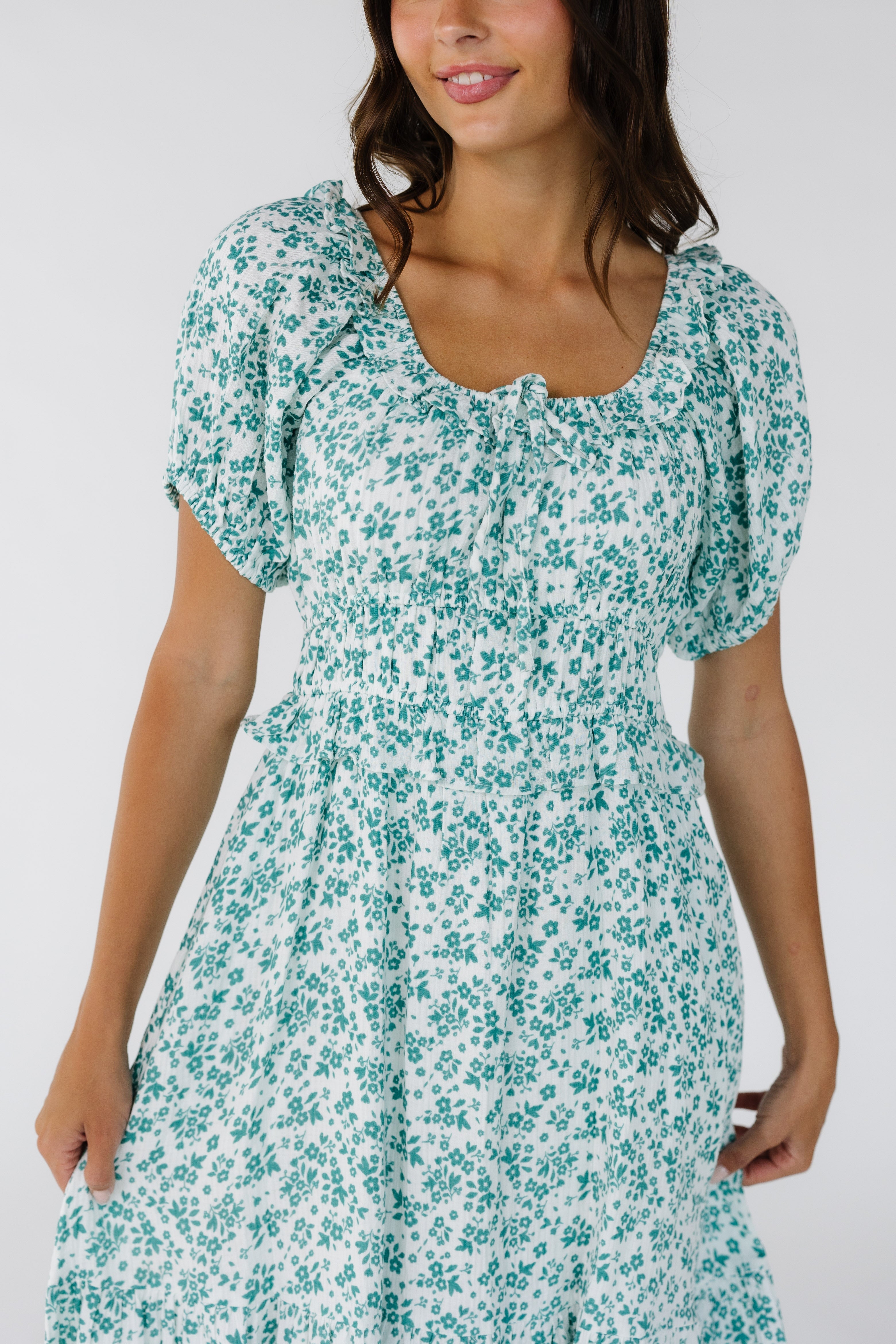 Close_view_of_a_woman_wearing_a_white_teal_dress_with_a_wide_waistband_with_a_bottom_ruffle_rufled_scoop_neckline_and_short_puff_sleeves.jpg Citrus Jena Print Dress