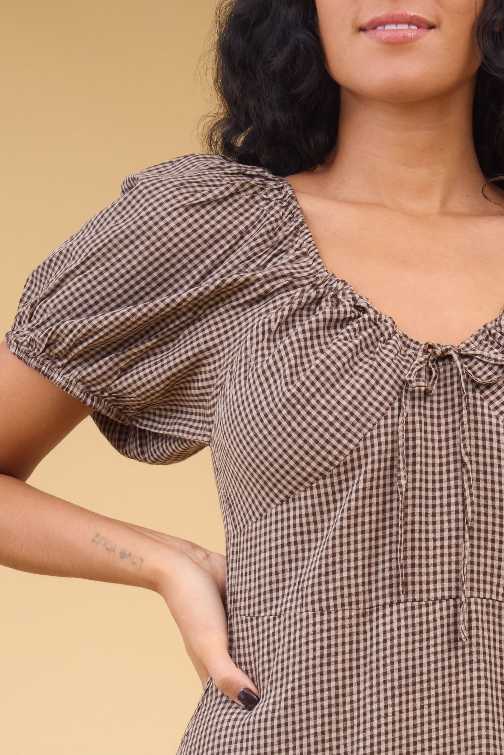 Close_view_of_a_young_woman_wearing_a_brown_gingham_midi_dress_with_short_puff_sleeves_sweetheart_neckline_empire_waist.jpg Citrus Alba Dress
