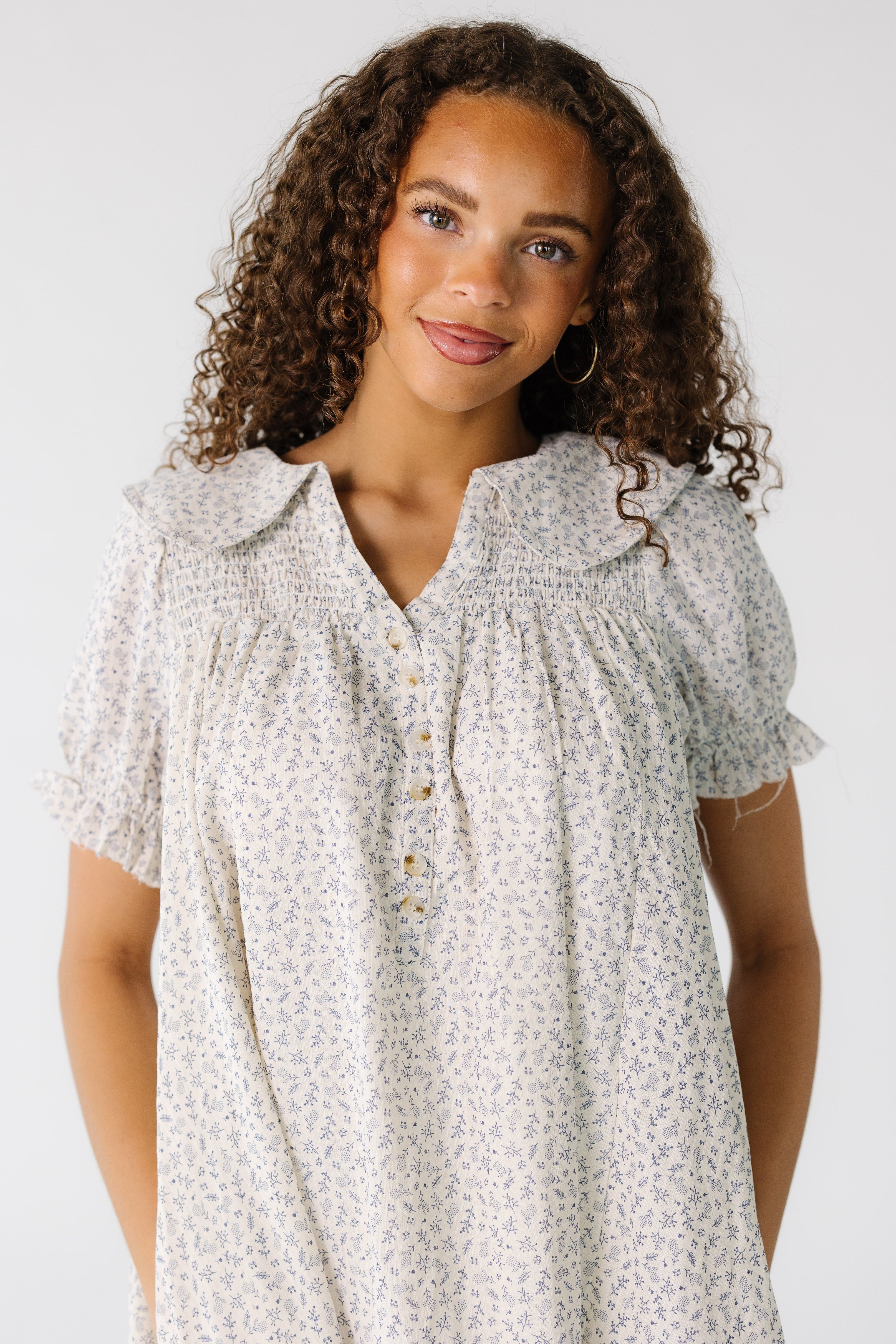 Closeviewofateengirlwearingawhiteandlightgreyprintdresswithawideroundedcollarandsmockedyokewithshortsleeves.jpg Brass & Roe Ditsy Collared Knee Dress