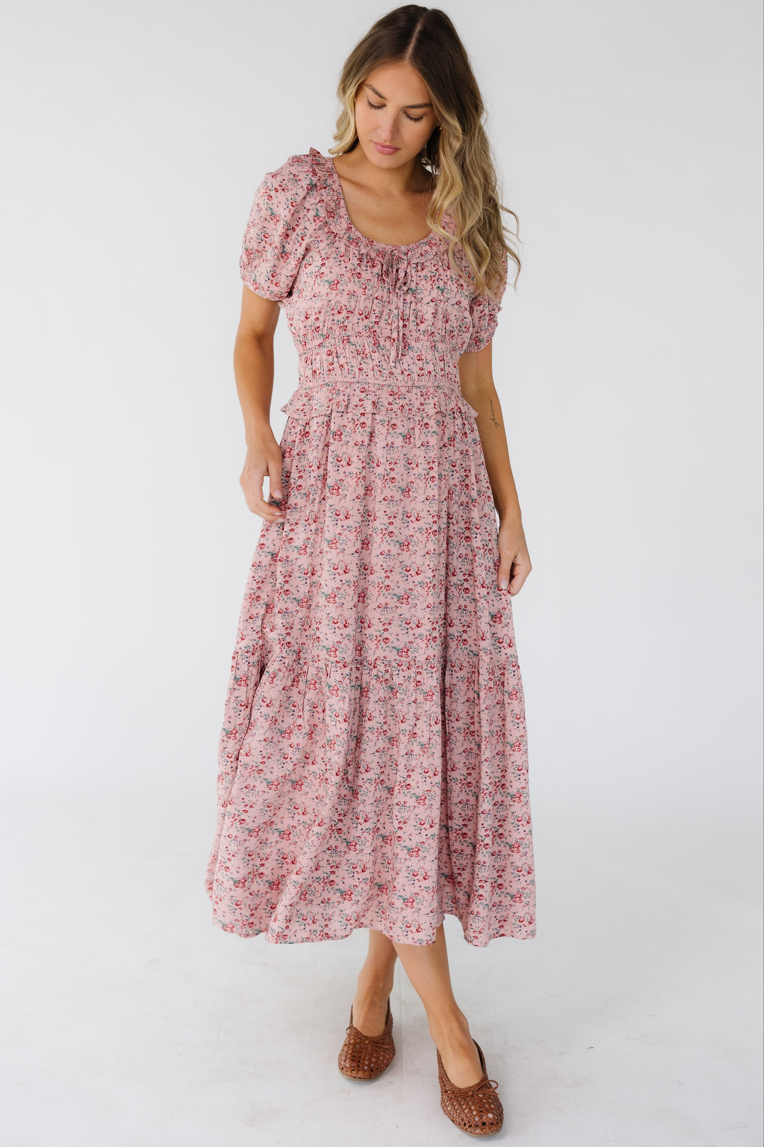 Young_woman_wearing_a_pink_floral_midi_dress_with_side_pockets_a_ruffled_scoop_neckline_wide_wasitband_and_short_puff_sleeves.jpg Citrus Jena Print Dress