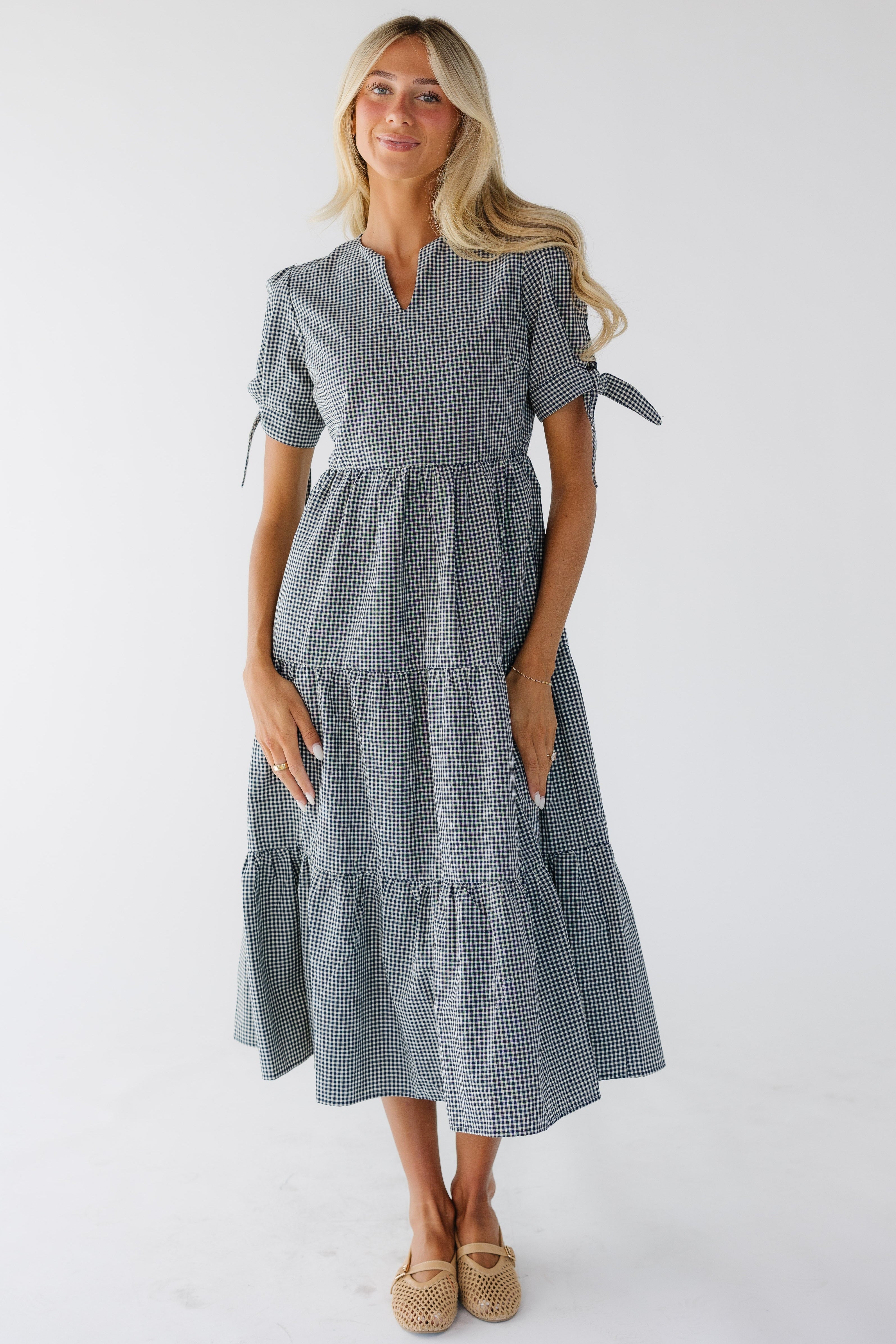 Youngwomanwearingamodestnavy_whiteginghamtieredmididresswithanotchedneckline.jpg Brass & Roe Claire Tie-Sleeve Dress